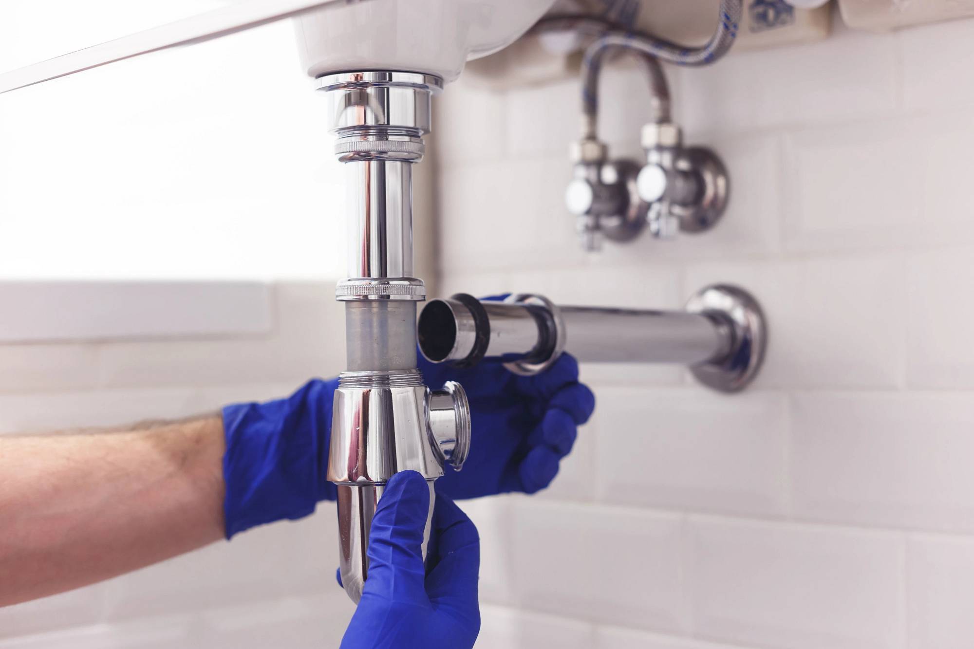 Plomero reparando tubería de drenaje bajo un lavabo